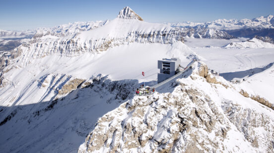 Modern building on a rocky, snow-covered mountain summit with panoramic views of surrounding peaks.