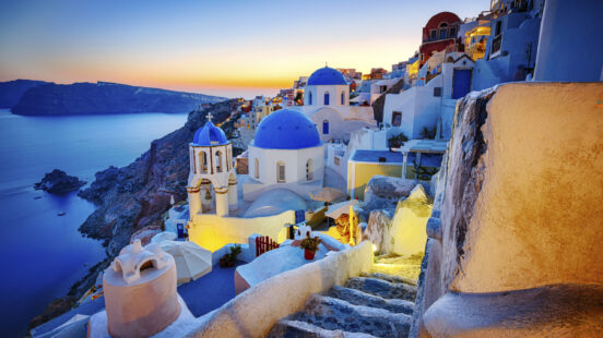 Blue-domed churches and white buildings of Santorini overlooking the sea at sunset.
