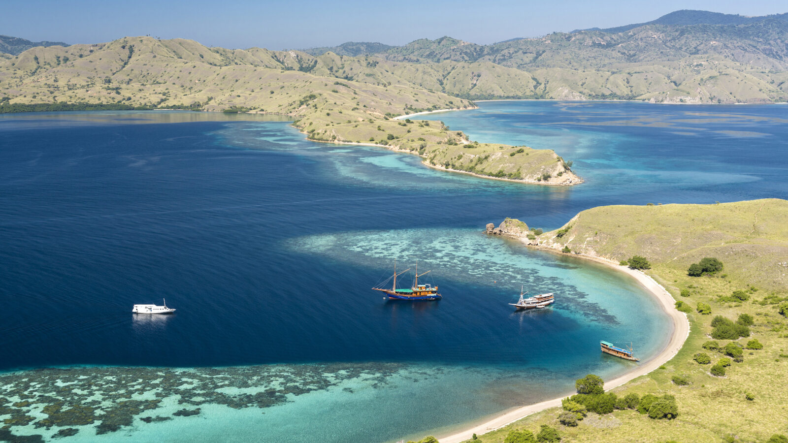 Aerial view of boats in a turquoise bay between tropical islands for Asia honeymoons.