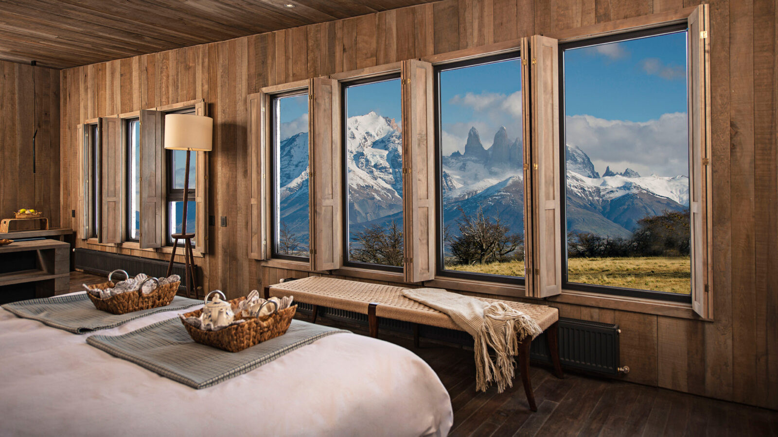 Villas Awasi Patagonia. A cozy wood-paneled bedroom overlooking snow-capped mountains on luxury Latin America honeymoon holidays.