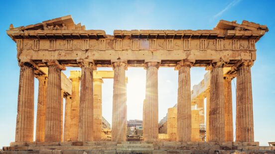 The sun shines through the stone columns of the ancient Parthenon in Athens, Greece.