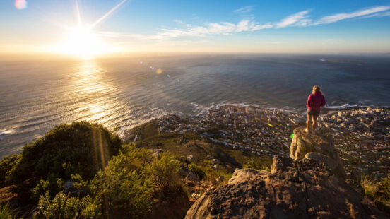 Silhouette of a person on a cliff watching the sun set over the ocean and coastline.