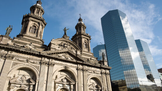 The classic Metropolitan Cathedral stands next to a modern, tall glass skyscraper in Santiago.