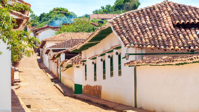 View up a steep cobblestone street lined with white houses and brown tile roofs under a clear sky.