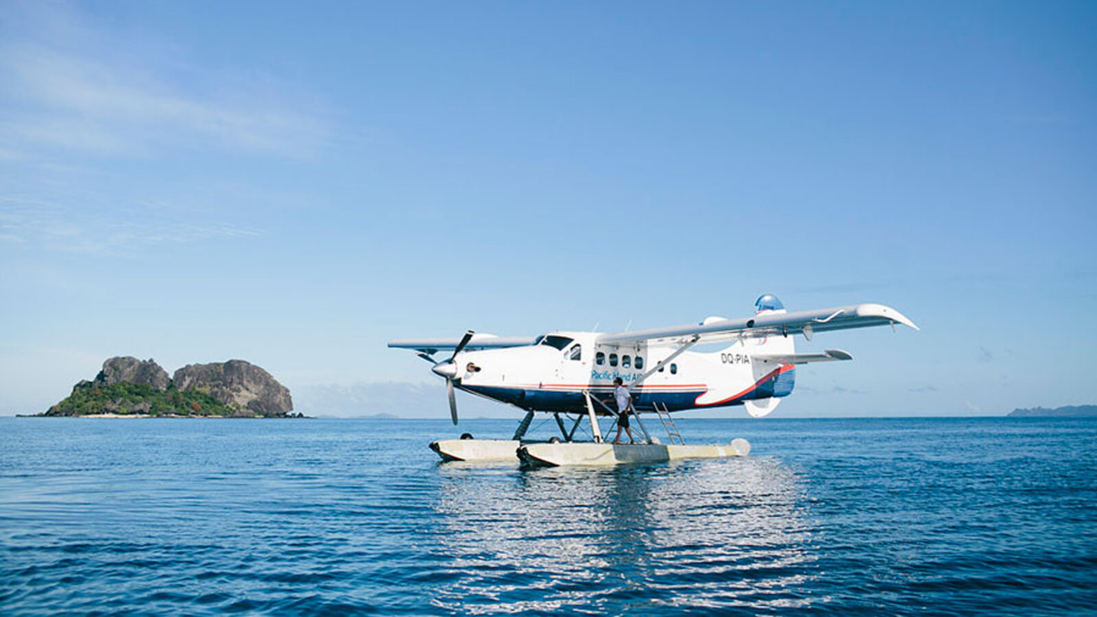 A smalls ea plane landed on the still calm water of the ocean with a small forested island in the background