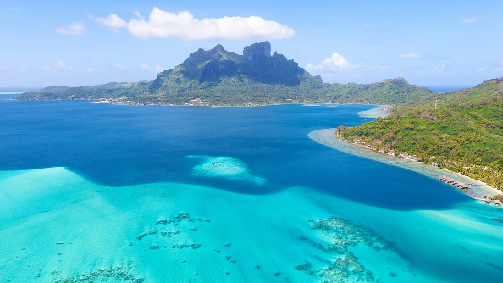 Aerial view of a tropical island mountain and turquoise lagoon during luxury French Polynesia holidays.