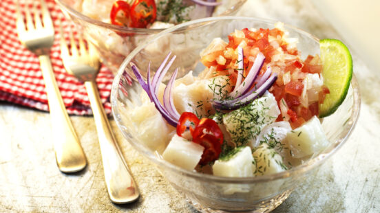 Glass bowls of seafood ceviche with citrus, red onion, and herbs on a rustic table.