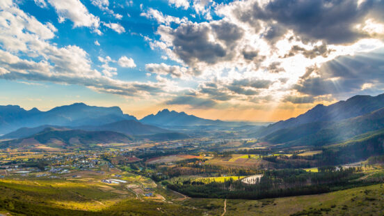 Sun rays shining through clouds over a vast mountain valley and rural landscape.