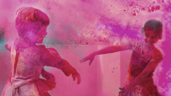 Two children playing amidst a thick cloud of vibrant pink celebration powder.