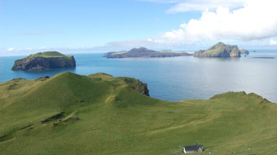 Rolling green hills of islands in the ocean with a small white building visible in the foreground.