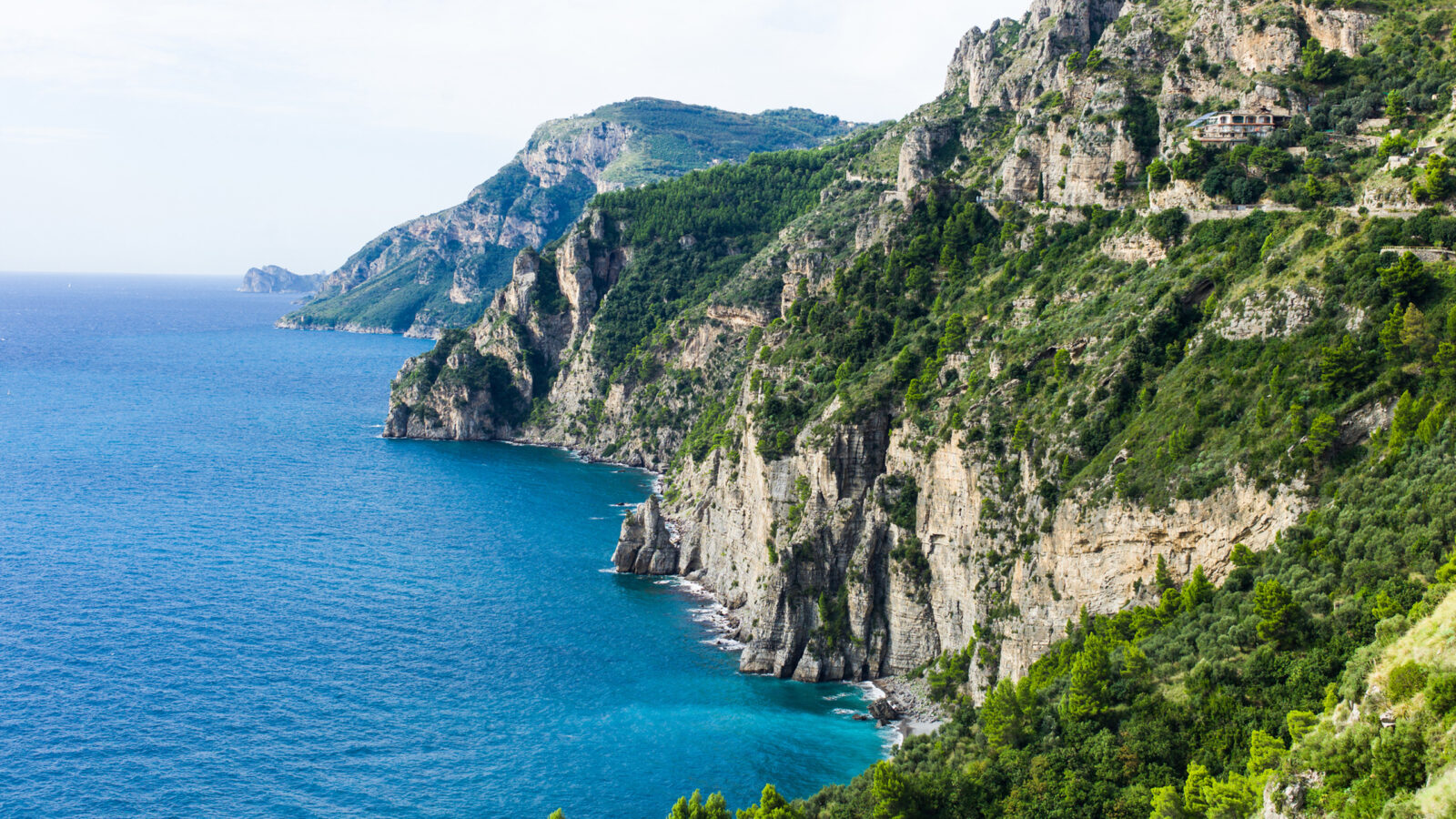 Towering green cliffs drop sharply into the deep blue Mediterranean Sea on luxury Amalfi Coast trips.