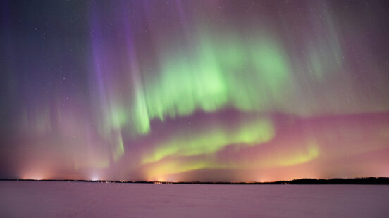 Bright green and purple northern lights stretching across a night sky over a dark, frozen horizon.