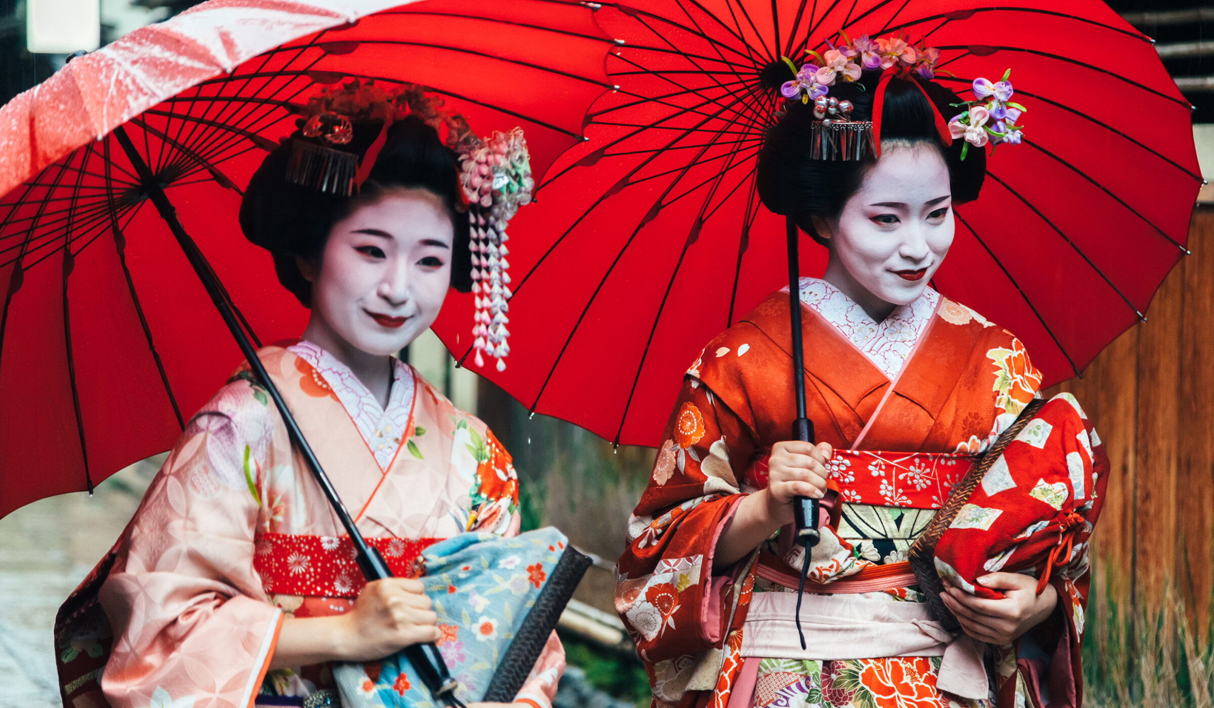 Private Japan Luxury Tours - Two maiko geisha walking on a street in Kyoto with red umbrellas