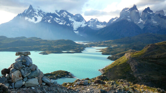 A cairn of rocks overlooks a wide view of a turquoise lake and the snow-capped mountains of Torres del Paine.