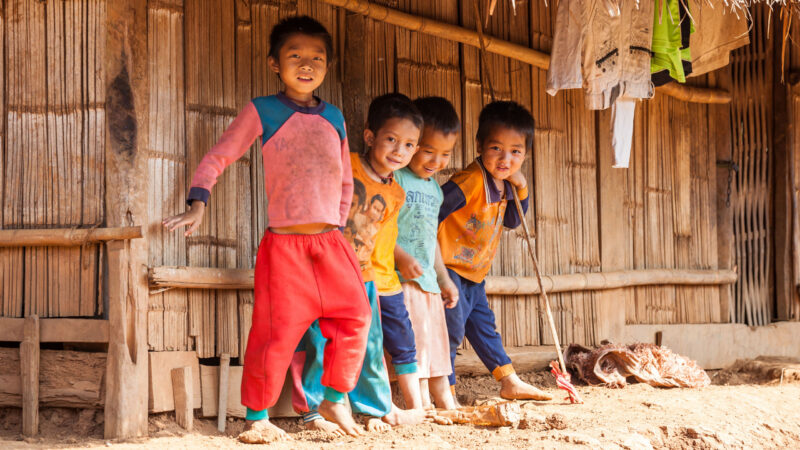 Hmong village near Luang Prabang, Laos – October 26, 2011: A group of kids from Hmong minority are standing in the shade of a traditional house in a hill tribe village near Luang Prabang, Laos