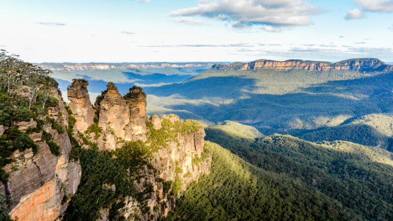 A scenic view of three large sandstone rock formations on a mountain ridge overlooking a deep, green valley.