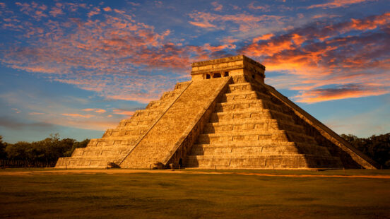 Large ancient stone step pyramid under a vibrant sunset with orange and blue clouds.