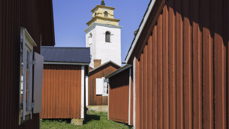 Old red wooden houses and Nederluleå church tower in Gammelstad church town in Luleå, Sweden, an UNESCO world heritage site.