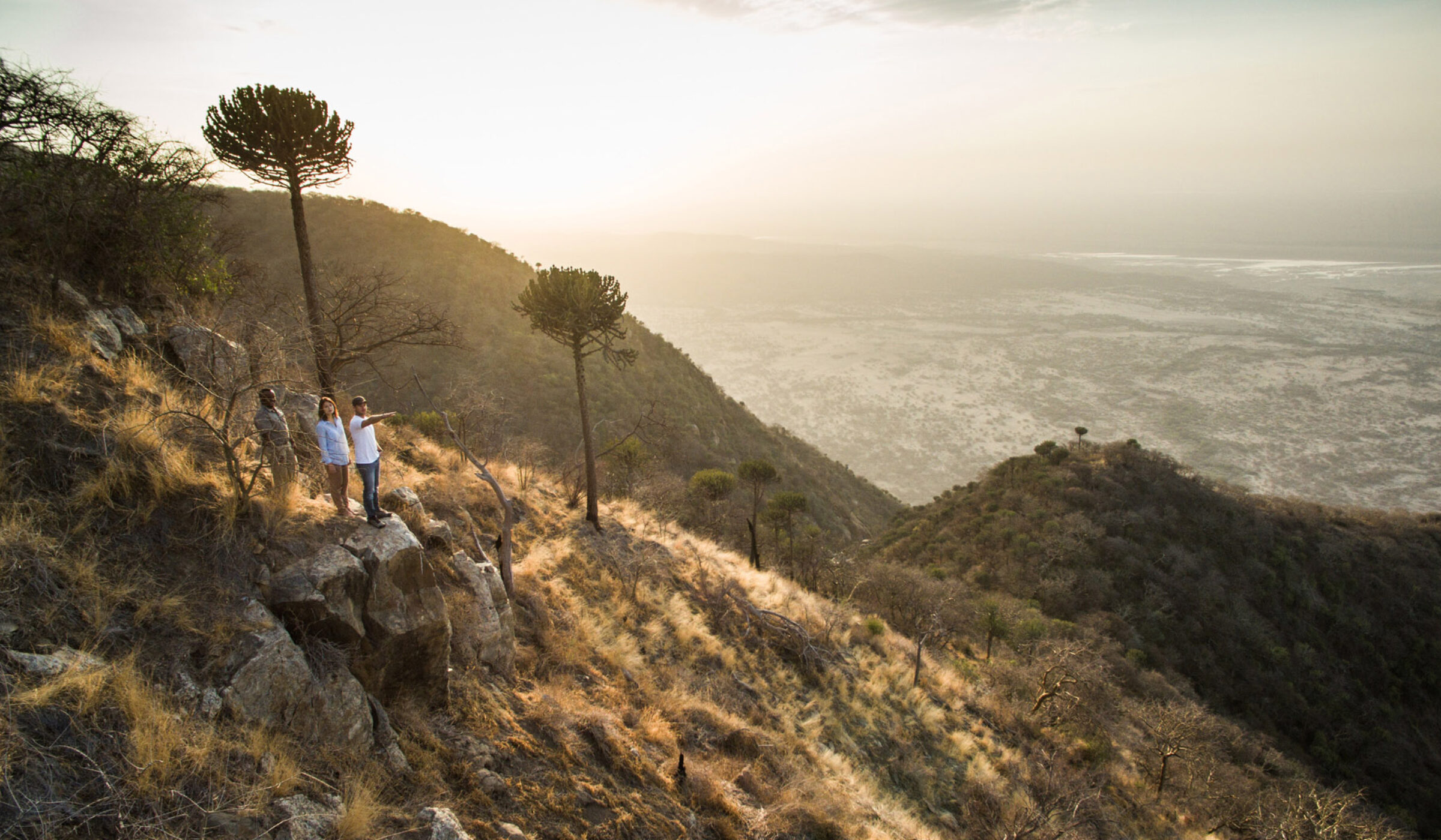 Travellers on rock edge looking out over a deep valley in Mwiba Wildlife Reserve, Tanzania