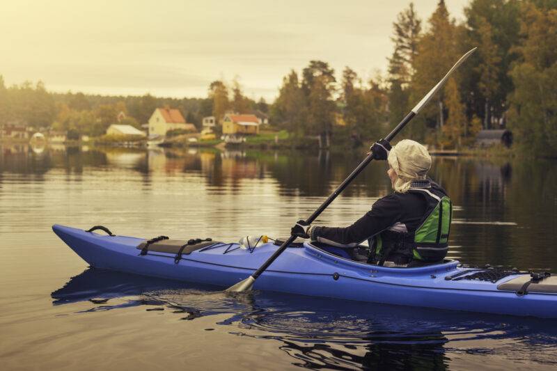 A senior woman out kayaking on a calm countryside lake in the morning.