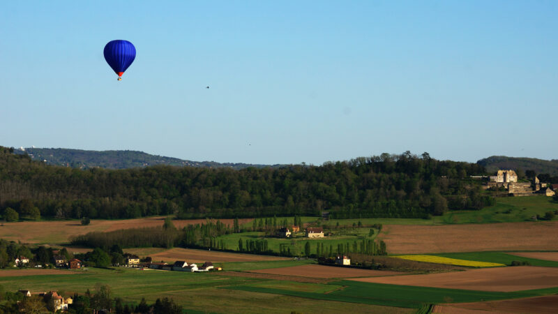 blue hot air ballon in the blue sky above dordogne valley in France, warm evening light, panoramic view over fleids and landscape