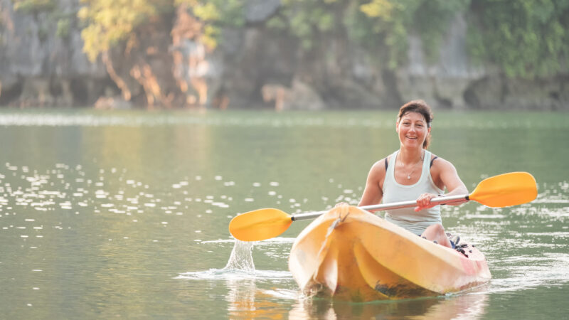 Morning kayaking – Eurasian woman paddling in front of remote Nam Cat Island, near Ha Long Bay, Vietnam