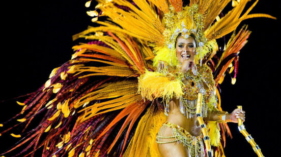 A person wearing a magnificent yellow and orange feathered headdress and carnival costume.