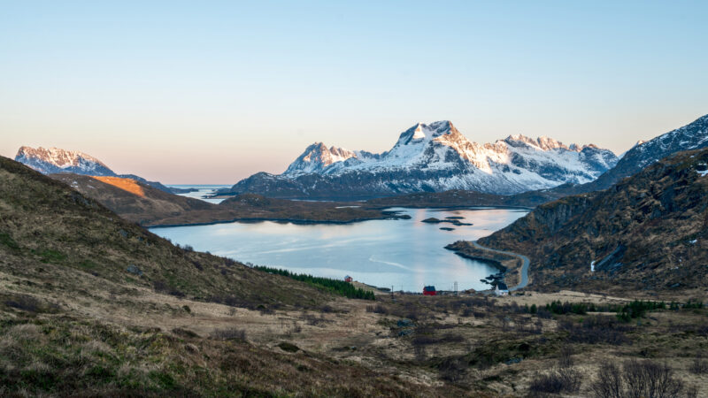 Landscape shot from the path towards Ryten in Lofoten/Norway looking south towards Reine during blue hour. Tiny houses and snow covered mountains in the background.