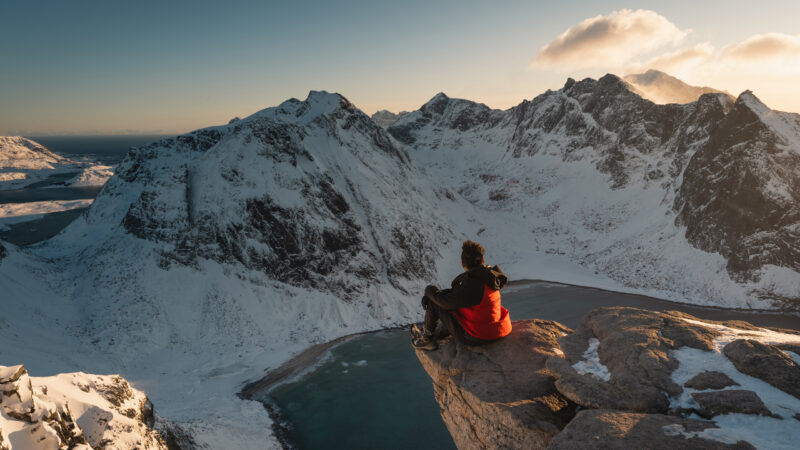 A hiker sitting in rock cliff on top of Ryten mountain peak in winter season, Lofoten island, Nordland Norway, Scandinavia, Europe