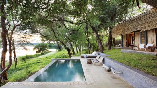 A modern lodge and swimming pool on a green hill overlooking a river.