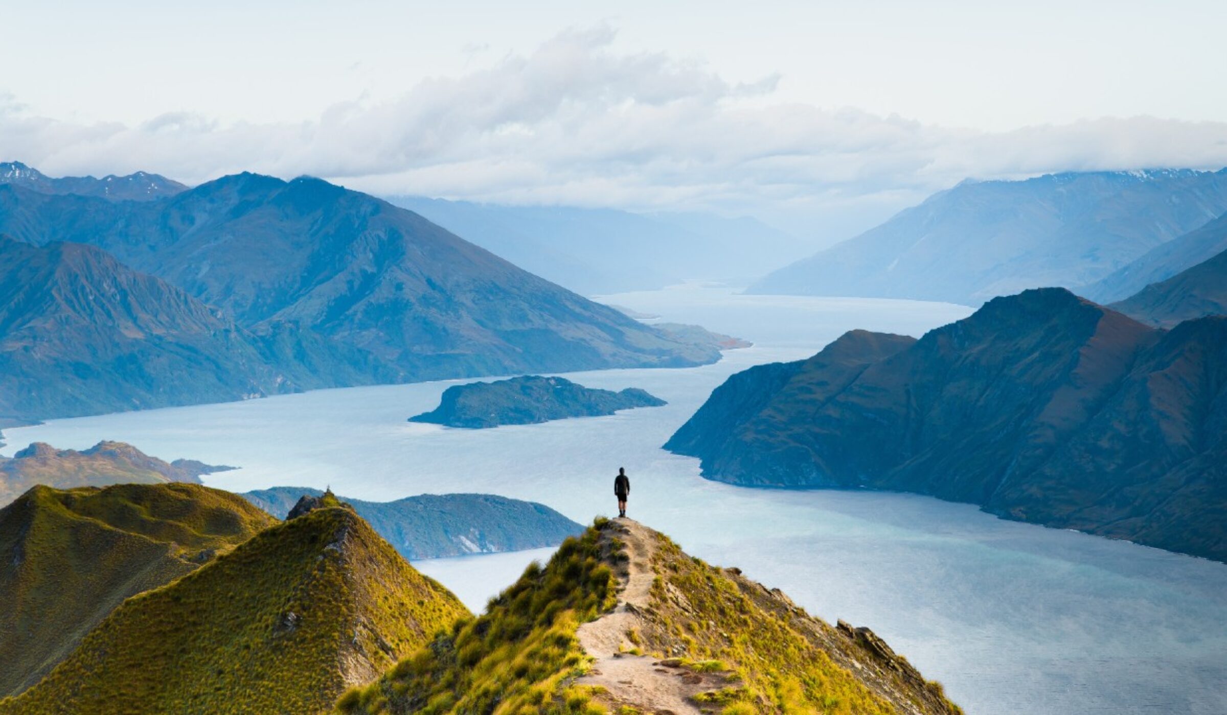 Two hikers walking on a trail through a deep green mountain valley with steep peaks in the distance, a luxury travel experience.