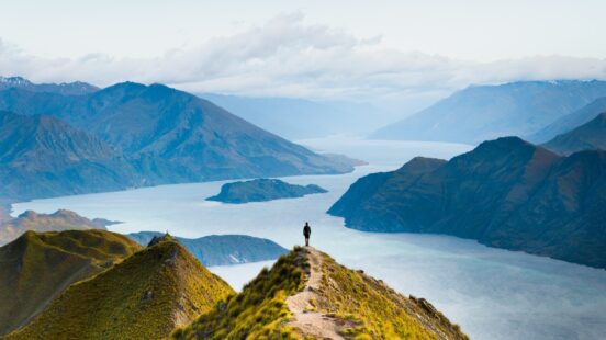 Two hikers walking on a trail through a deep green mountain valley with steep peaks in the distance, a luxury travel experience.