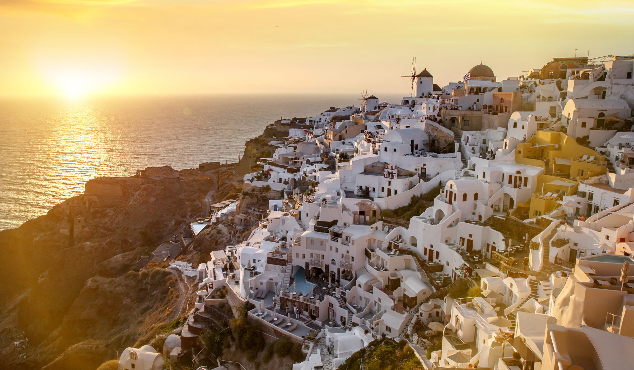 Golden sunset over the white hillside buildings and windmills of Santorini, a dream for luxury Honeymoons.