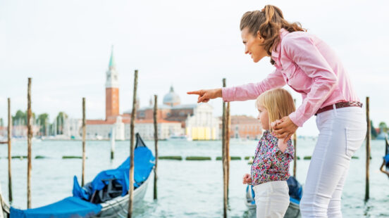 Mother pointing baby on something on grand canal embankment in venice, italy
