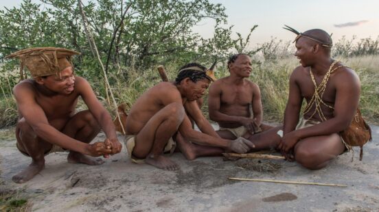 A group of men in traditional tribal clothing crouching on the ground, smiling, and laughing