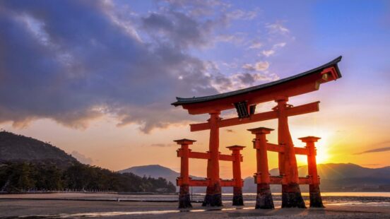 Itsukushima’s vermilion torii gate stands at low tide, sunset on Miyajima.