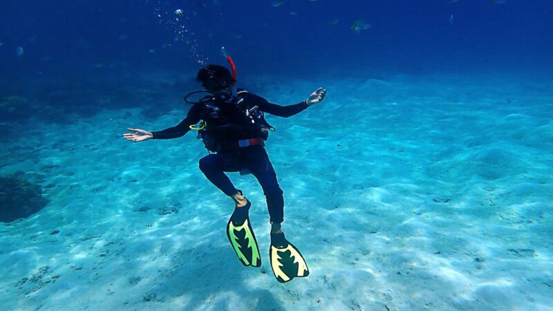 Scuba diver with yellow fins swimming over a sandy ocean floor during luxury Borneo tours.