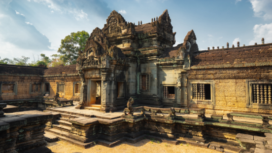 Detailed stone ruins of an ancient Khmer temple featuring intricate carvings and balustraded windows.