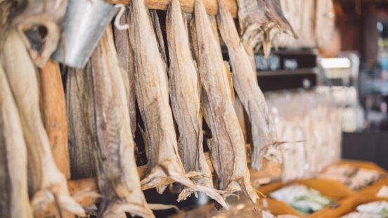 Close-up of traditional dried stockfish hanging from wooden poles in a market.