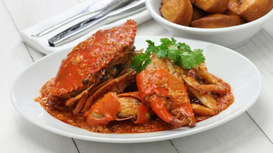 A white plate of Singapore-style chili crab with fresh cilantro garnish and a side of fried buns.