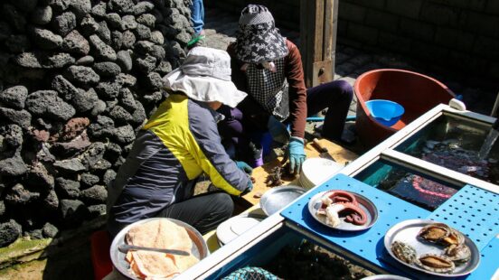 Two people cleaning fresh seafood into metal plates at an outdoor workspace.