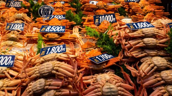 Rows of fresh snow crabs on ice at a seafood market with blue price tags in Japanese Yen.