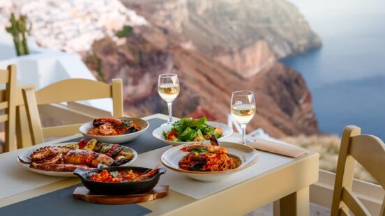 Seafood spread with grilled octopus, pasta, and salad on a table overlooking the sea in Santorini, Greece.