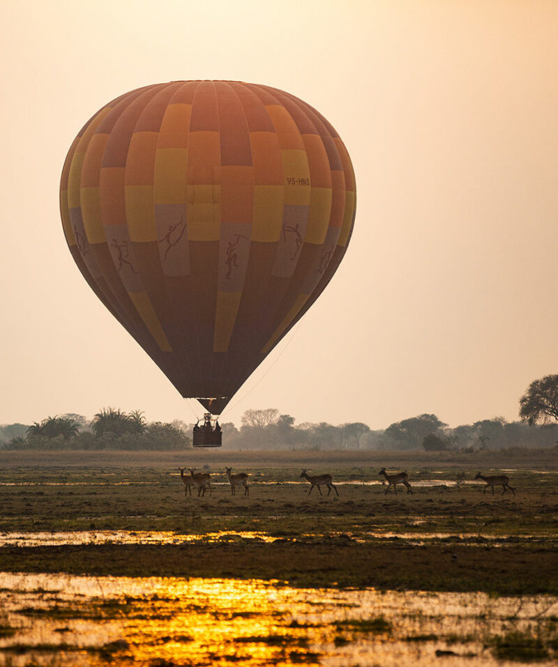 Hot air balloon flying over a landscape with wildlife during luxury Zambia trips.