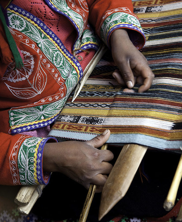 Luxury Peru Tours - A woman's hand weaving traditional, colourful wool fabric in Peru