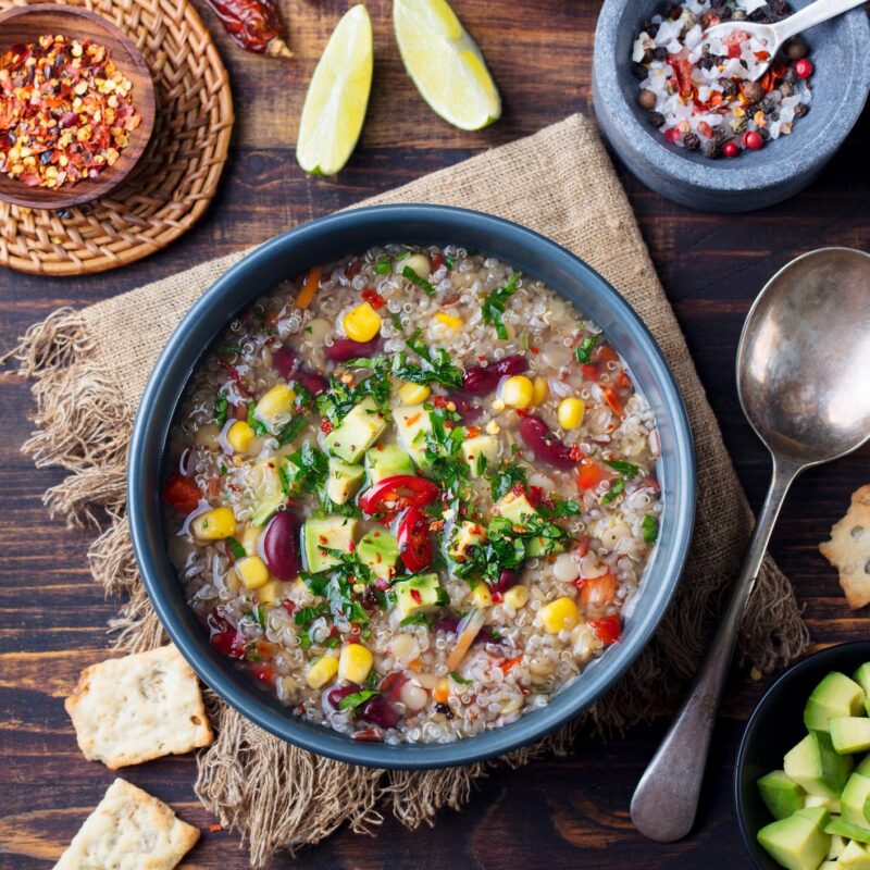Overhead shot of a bowl of colorful quinoa soup with corn, beans, avocado, and lime wedges, part of Luxury Colombia Trips.
