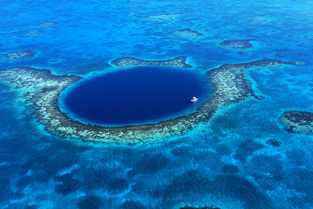 Aerial view of the Great Blue Hole, a large, deep blue, circular sinkhole surrounded by a shallow coral reef. Essential for luxury Belize tours.