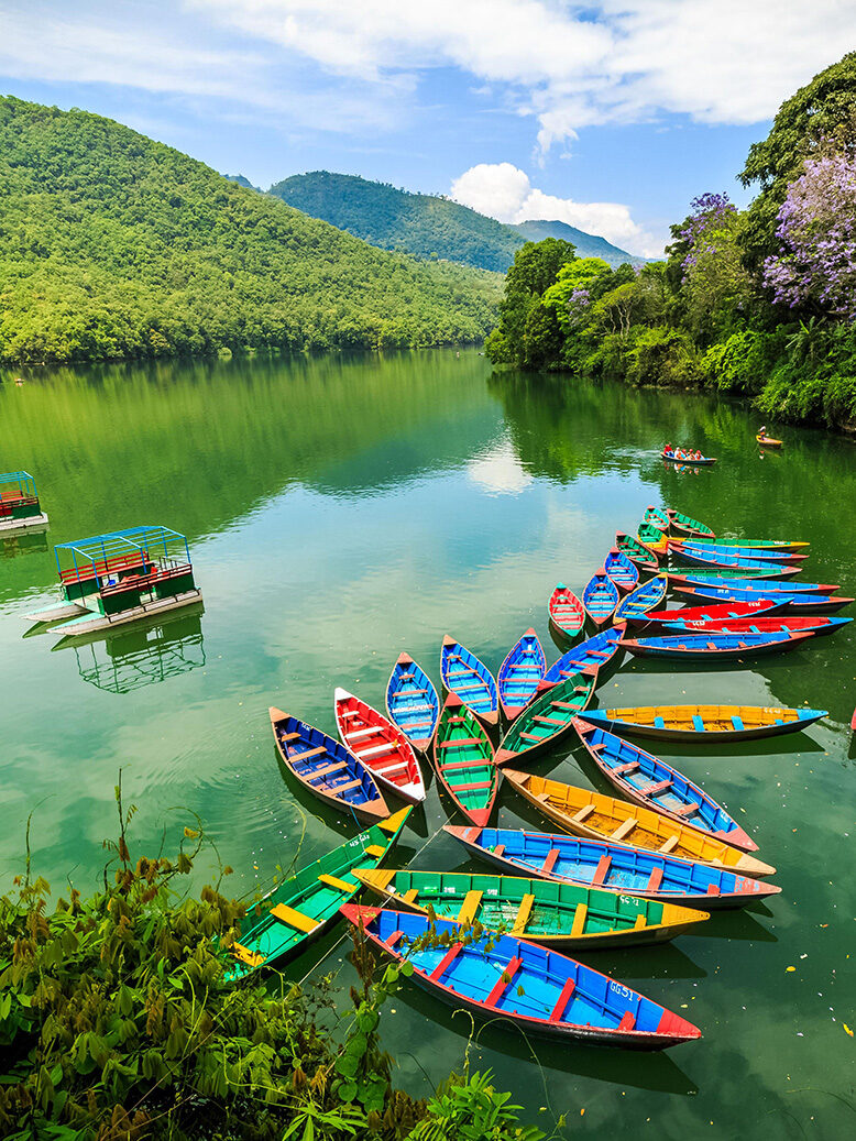 Colourful boats moored in still water in a lake with forested mountains around