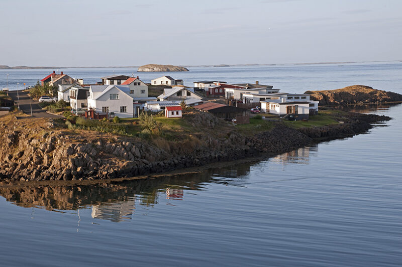 Small white and colorful houses stand on a rocky peninsula surrounded by calm, reflecting water, ideal for luxury Iceland holidays.