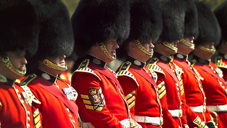 British Foot Guards in red tunics and tall black bearskin hats standing in a close, military formation.